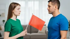 Žena drží červenou vlajku před mužem, symbol varování v partnerském vztahu.