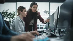 Dvě ženy pracují u počítače v moderní kanceláři, spolupráce a pracovní prostředí.