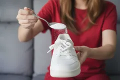 Žena sype prášek do bílé tenisky pro odstranění zápachu z bot.