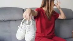 Žena držící páchnoucí boty, zacpává si nos na šedé pohovce, zápach obuvi doma