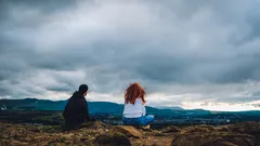 Muž a žena sedí na vrcholu kopce při západu slunce