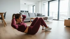 Žena provádí sedy-lehy doma v obývacím pokoji, cvičení na posílení břišních svalů.