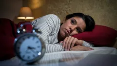 Žena s nespavostí leží v posteli a sleduje budík v noci, problém se spánkem