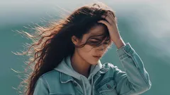 Žena s dlouhými vlasy v džínové bundě drží ruku ve vlasech venku ve větru