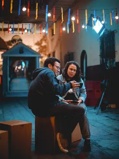 Muž a žena sedí na lavičce a dívají se na mobil
