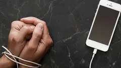 Ruce svázané kabelem od telefonu, symbolizující závislost na mobilním zařízení.