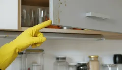 Úklid kuchyňské skříňky, ruka v gumové rukavici ukazuje na špinavé dvířka