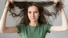 Žena s dlouhými rozcuchanými vlasy v zeleném tričku drží vlasy od hlavy