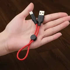 Krátký červený USB kabel na ruce, vhodný pro nabíjení a přenos dat