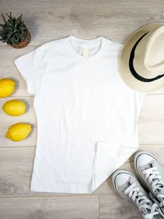 Bílá tričko s kulatým výstřihem na dřevěné podlaze vedle tenisek, citronů a klobouku